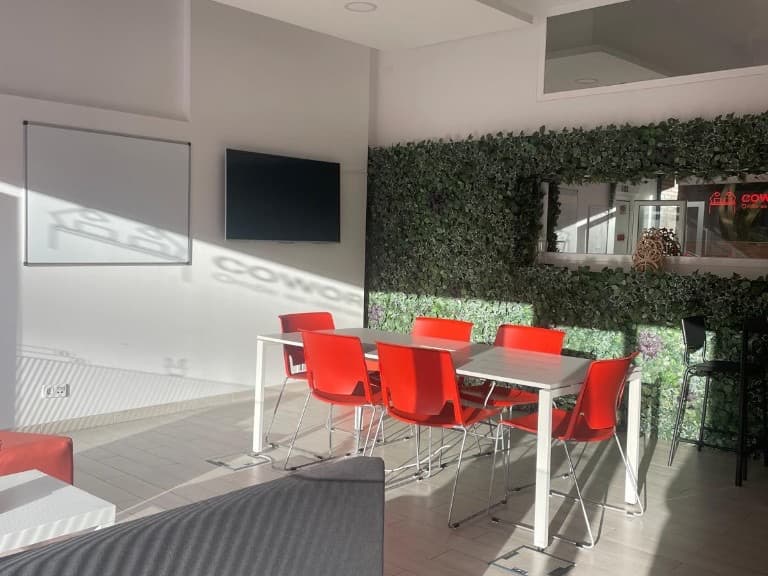 Sala Alverca no Cowork Malvarosa, mesa branca, cadeiras vermelhas, quadro branco, televisor e parede verde