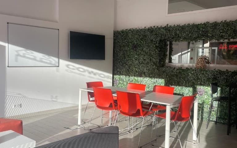 Sala de reunião no Cowork Malvarosa, mesa branca, cadeiras vermelhas, quadro branco, televisor e parede verde